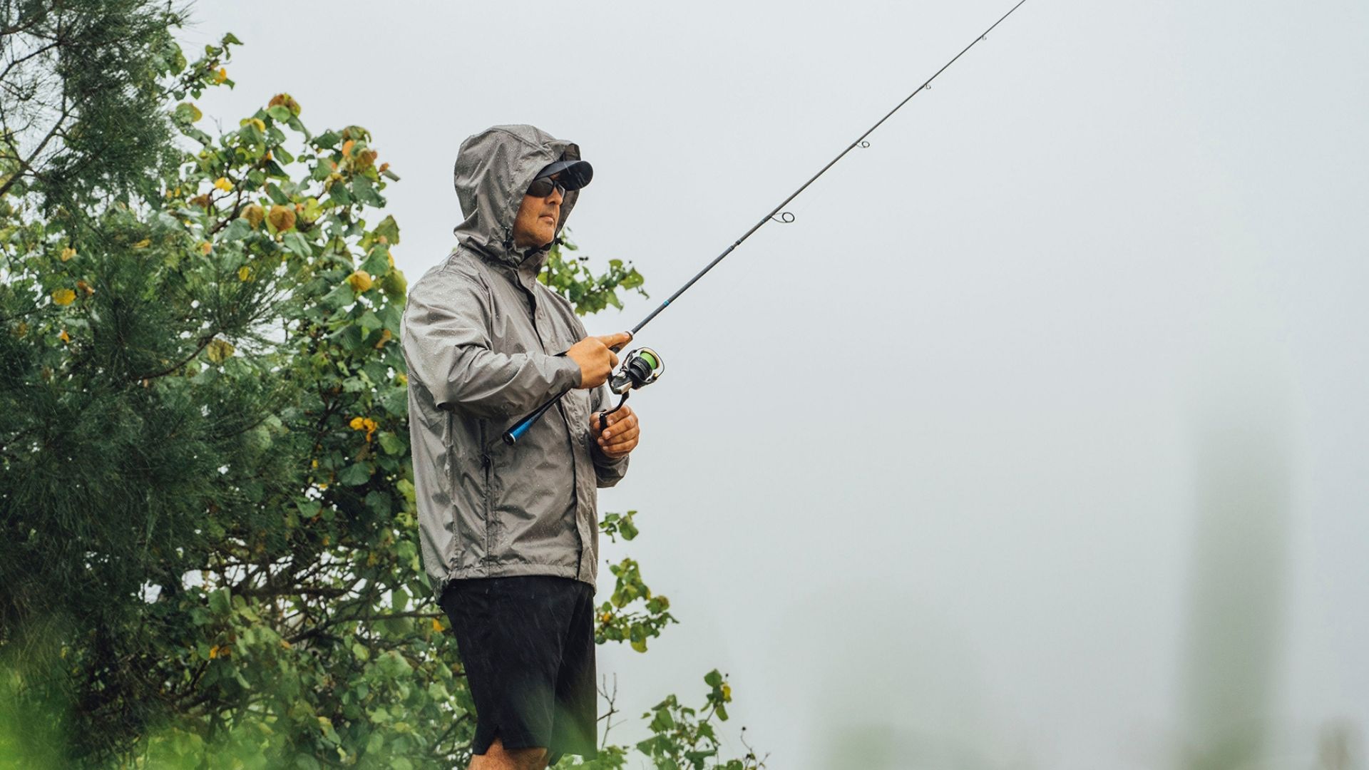 Man wearing sunglasses, cap and hooded waterproof jacket fishing