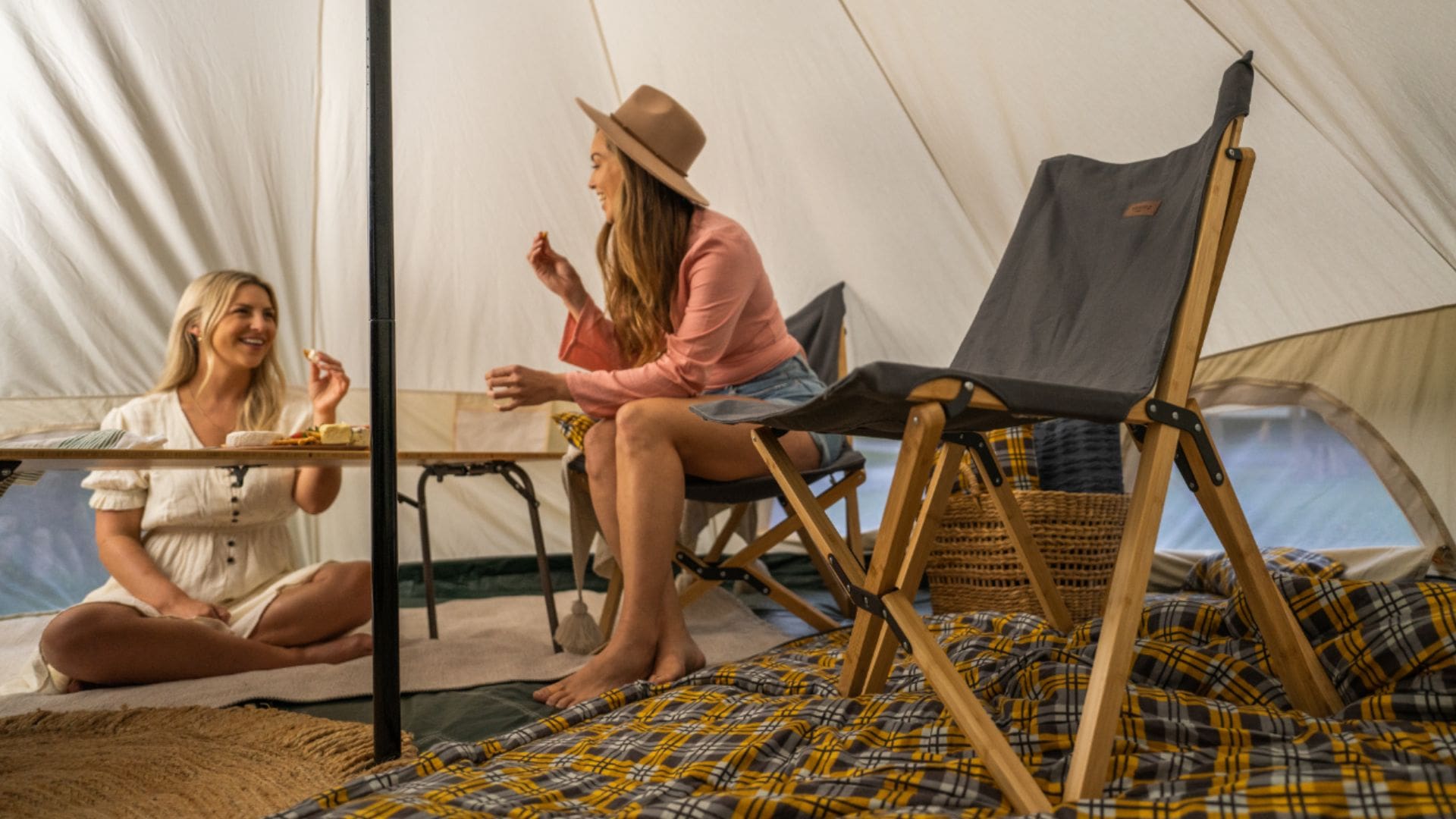2 women eating a cheeseboard in a large furnished beige tent