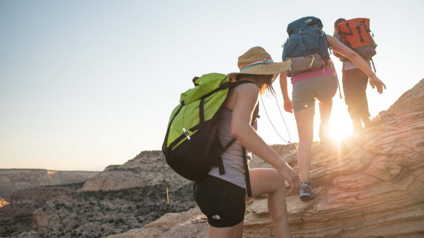 3 Hikers climbing up rocky terrain during sunrise