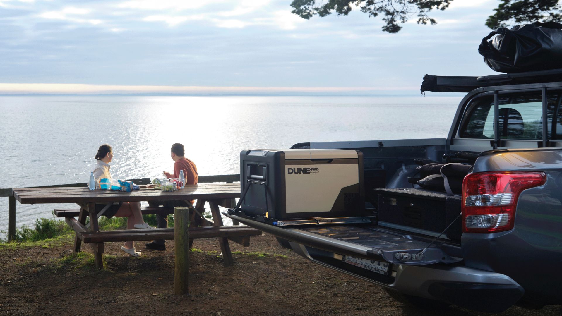 2 People enjoying ocean view from a park bench with a DUNE 4WD 45L Single Zone Fridge/Freezer